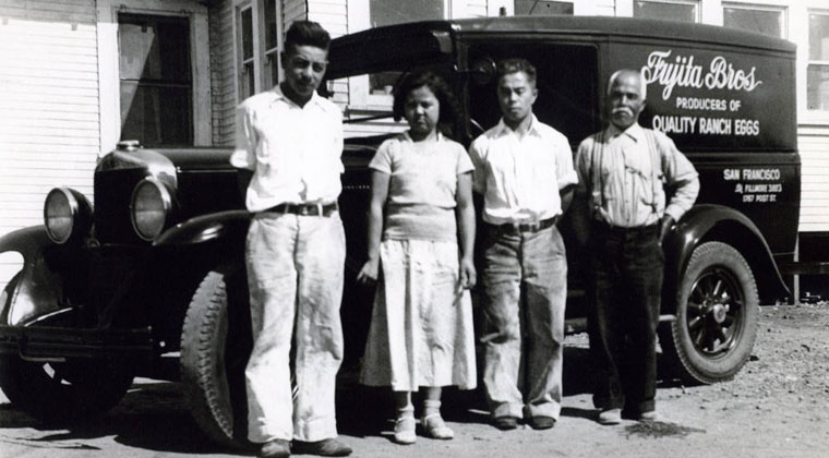 Delivery truck parked in front of a building.  Four people are in front fo the truck.