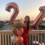 Woman holding up 2 ballon's, one is a 2 the other is a 1