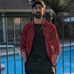 Man wearing black pants and shirt with a red checkered overshirt.