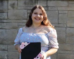 Smiling woman, holding a decorated diploma container.