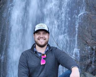 man kneeling in front of waterfall.