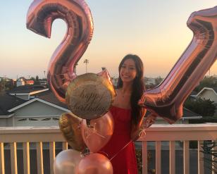 Woman holding up 2 ballon's, one is a 2 the other is a 1