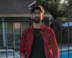 Man wearing black pants and shirt with a red checkered overshirt.